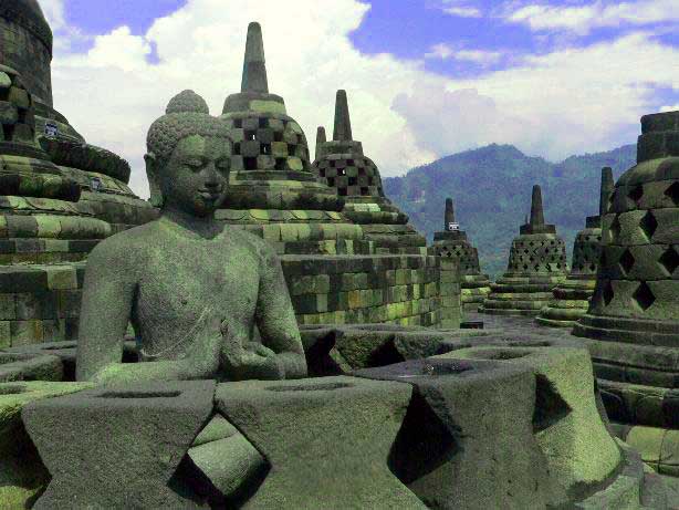 Borobodur and Prambanan

Though I love temples I seldom get the chance to  go to temples outside India. So I was very happy to get an invitation from my Japanese daughter to go to Indonesia  to visit the ancient temples of Borobudur and Prambanan.  Thus it happened that I landed in  Jakarta last week and took the next flight to Yogjakarta. This city is also known simply as Jogja or Yogya. This word is actually a corruption of Ayodhya, the famed city of Rama in India. Names from the Ramayana abound in this island. Sometimes even without their knowing it many of the names used by the Indonesians are Sanskrit in origin but of course most of them are so distorted that it takes a while to find out the actual source.  The Special Region where Yogyakarta is situated is the smallest province of Indonesia (excluding Jakarta). It is located on the island of Java. The word Java has such a special flavour that I was really glad that I had come here instead of one of the big cities. On a clear day one can see the famed volcano Mt. Merapi, which is still alive and the history of which is closely connected with the history of Borobudur and Prambanan.  
 This 300 hundred old city is the cultural centre not only of Java, but of the whole of Indonesia. This is in part due to the variety of religious influences found here like, Buddhist, Hindu, and other indigenous beliefs, which resulted in the construction of the impressive temples of Borobudur, Prambanan and the Dieng temple complex. 
Indonesia's oldest palace 'The Kraton,' is situated here. This is still the home of Jogya's royalty. It is the only province in Indonesia that is still formally governed by a Sultanate, the Sultanate of Ngayogyakarta Hadiningrat. Even now the current Sultan of Yogyakarta retains remarkable political prestige. Yogyakarta offers an abundance of Javanese art, painting, silverwork, batik handcraft, traditional Javanese dances, as well as contemporary art. 
From Yogyakarta airport we took a taxi to Borobudur where we stayed at the Manohara hotel which is supposed to be the only one with a magnificent view of the temple which can be seen right in front of it. The hotel is set amidst a typical tropical garden filled with lush greenery and the usual tropical flowers like ixora, frangipani, bouganvilleas in variegated shades, sweet smelling jasmine and the famous paritjata flower which is mentioned in our puranas. There was a unique blend of cultures even in the décor. We were greeted by two ancient Ganesha statues at the entrance but there was a pool in front of the hotel in which you found a statue of Lakshmi which had a striking resemblance to the Chinese goddess of prosperity called Kuan Yin and scarcely any resemblance to the Hindu goddess.  At night four huge water lilies bloomed, shedding their intoxicating fragrance into the air. I had read about these night blooming water lilies called 'kumudini' in Sanskrit literature but it was the first time that I had ever seen them. They were pure white and as big as lotuses. They reached their maximum size at midnight and closed up again by morning.
Watching the sunrise from the top of the temple was supposed to be a great experience but again we were told that since it was the rainy season it was very unlikely that we would be able to see it. I breathed a sigh of relief that I wouldn't have to jump out of bed at 3 in the morning and dash up the hill. I had been traveling continuously from 4 am the previous day. It was a grueling journey from Rishikesh to Delhi and from Delhi to KL and then to Jakarta and to Yogyakarta and finally to Borobudur!!
However we set off at 10 in the morning along with a host of other sight seers. They were certainly not pilgrims and all of them were armed with hats and caps of various sizes and designs and of course the umbrella man was having a great trade selling multi colored umbrellas. So armed with one of these I set off in the blazing hot sun, not waiting for the rest of the party who were frantically searching for a good guide. Since I was a very slow walker and even a slower climber I fully expected the young members of my party to catch up with me in no time. But I climbed and climbed for more than half an hour without seeing any of them. Each time I turned round to have a look, all I could see was a sea of brightly colored umbrellas bobbing up and down. Eventually I gave up the attempt and decided to carry on to the top on my own. I did two of the pradikshanas or circumambulations of the 5th and 6th platforms and finally reached the top to get to which one had to climb some steps which were obviously made for giants. I was totally drenched in perspiration and would have been glad to get at least a tiny bit of shade but there was none to be had since all the pagodas hardly cast any shade as it was 12 noon. As I stood in the blazing hot sun, not knowing whether to go back or wait for the party, a number of college students clustered round me and started to talk to me very eagerly. They were so sweet that despite the heat I stood and answered all their questions. They had some sticky Indonesian sweets which they pressed on me. I was forced to take some even though the thought of eating sticky sweets when my whole body was sticky and hot was not a very happy thought. Before we parted they presented me with a pearl rosary and of course I gave them our ashram cards with the photo of baby Krishna by which they were quite charmed. I realized afterwards that this is typical Indonesian behavior. They are such a charming people, so friendly, so polite and so interested in people from India.  I started my journey back to the ground soon after since I realized that unless I got to a shade soon I would probably collapse from the heat.
Now to describe the temple….  If seen from the air and also from the small reproduction of it in the museum I realized that it was made in the form of a Hindu Meru which is a vertical representation of the Sri Yantra. Apparently this was the shape of a Buddhist mandala. The height of the whole edifice before renovation was 42 meters. Now it is only 34.5 meters  since the lowest level has been used as a supporting base.
 It has ten terraces. The first six terraces are square and the two upper terraces are circular. Right on top is the terrace on which the statue of the Buddha had been seated facing westward. The statue has been removed and is now to be found in the museum. Each terrace symbolizes one of the stages of human life.  The aspirant who wants to reach the stage of the Buddha has to go through each of these stages. The base is known as Kamadhatu. There is a very similar square in the Sree Yantra which is supposed to be that state of life in which the human being is still bound by desires 'Kama' and passions. From here we climb up to the second, third and fourth terraces and these are known as Rupadhatu. This is the stage when the human being is still bound to 'rupa' or form that is to the world of shapes and forms - the world of the senses as we experience it. On these four terraces the effigies of the Buddha are placed in open space. The next three terraces are known as Arupadhatu and here the effigies of the Buddha are confined inside domes with holes in them. Only those who have freed themselves from lust and passion for forms, can reach this stage. The final part is known as Arupa and is the state of nirvana, or liberation which is the state of the Buddha 
Borobudur is said to have been built by King Samaratungga, one of the kings of the old Mataram Kingdom, the descendants of the Sailendra dynasty. Based on Kayumwungan inscription, an Indonesian named Hudaya Kandahjaya had a revelation in which he was told that Borobudur had once been a place for prayer that was supposed to be completed  on 26 May 824, almost one hundred years after the construction had started. The name of Borobudur, as some people say, means a mountain having terraces (budhara), while other says that Borobudur means monastery on a high place. 
It is a  Buddhist temple and has 1460 relief panels and 504 effigies of Buddha in its complex. These panels are all on the walls of the terraces. In order to see them one has to climb the stairs of each of the terraces and then do a pradikshina  or circumambulation in a clockwise direction round it. This is the correct way to discover the beauties of the temple and also derive maximum spiritual benefit.
Each terrace has its own panels showing how skillful the sculptors were. Some of these panels tell the legendary story of the Ramayana. Besides these, there are panels depicting the condition of the society at that time.  Some show farmers working in the fields and some show sailors in boats, thus giving us a glimpse of the advanced state of the navigation techniques of that age.
Many of the panels reflect the Buddha's teachings. If you walk through each narrow passage in Borobudur with a competent guide you will come to know much of the philosophy of Buddhism. Atisha, a Buddhist monk from India in the tenth century once visited this temple that was built 3 centuries before Angkor Wat in Cambodia and 4 centuries before the Grand Cathedrals in Europe. After gathering a lot of information from these reliefs he returned to India and started another sect known as Vikramashila Buddhism. Later he became the leader of the Vikramashila monastery and became a teacher in Tibet. Six scripts from Serlingpa were then summarized as the core of the teaching called "The Lamp for the Path to Enlightenment"  known as Bodhipathapradipa.
The scupture of the panels leaves you spellbound. Great attention is paid to the most intricate details. Some portions show what happens to those who do evil deeds and what happens to those who do good deeds. Buddha's dictum was that karma or action alone decides our life both now and in there hereafter. 'As we sow, so we shall reap.'
Some of the panels depict the 'Jataka Tales' in which moral questions are answered  through beautiful tales of birds and animals.
The mystery of why the temple was constructed in the first place and how it was buried for centuries is still not clear. Some say that initially it was surrounded by swamps and was buried because of the volcanic eruption of Mt. Merapi. 
Sir Stamford Rafles was said to be the one who first discovered the existence of this site and encouraged a German to excavate the huge mound and unearth the wonders of this temple. Since then the Indonesian government as well as the UNESCO has done a lot of restoration on the temple which is still being carried on. However when you go there in the early morning, you can have a glimpse of what it might have been in ancient times. The edifice looms through the pearly mist of a monsoon day and one can imagine the wonder and the mysery of that amazing place and imagne the ancient Buddhist pilgrims plodding their way up with their rosaries swinging from their hands muttering the great mantra of the Buddha - 'Aum Mani Padme Hum'. 
 

PRAMBANANA TEMPLE
We left Borobodur reluctantly and returned to Yogjyakarta.  Our next port of call was Prambanan which is a ten-century Hindu temple. This temple is dedicated to Shiva, and is locally known as Candi Loro Jonggrang, which means 'temple of the slender virgin.' The beautifully sculptured spire, of the main temple which soars up to a height of fifty meters  does indeed resemble a 'slender virgin.' Like the Buddhist stupa in Borobudur , Prambanan was probably abandoned when the Buddhist and Hindu inhabitants of Java moved to East Java. The temple is situated seventeen kilometers east of Yogyakarta, and is believed to have been built by King Balitung Maha Sambu in the middle of the ninth century. Another story goes that it was built around 850 CE either by Rakai Pakatan of the second Mataram dynasty, or Balitun Maha Shambu, during the Sanjaya Dynasty. Not long after its construction, the temple was abandoned and began to deteriorate. This was no doubt due to some fault in the location of the site according to Vaastu - the Indian science of architecture.Reconstruction of the compound began in 1918. The main building was completed around 1953. Much of the original stonework had been stolen and used at other sites. A temple will only be rebuilt if at least 75% of the original stones are available, and therefore only the foundation walls of most of the smaller shrines are now visible and there are no plans for their reconstruction.
The temple was again severely damaged during the earthquake in Java in 2006. Early photos suggest that although the complex appears to be structurally intact, damage is significant. Large pieces of debris, including carvings, were scattered all over the ground. The temple was closed to the public for  quite a while. However, some weeks later in the same year the site re-opened for visitors.
The temple complex is set like a jewel amongst luxuriant green fields and some villages. It has eight shrines, of which the three main ones are dedicated to the trimurtis, Shiva, Vishnu and Brahma. The main temple of Shiva rises to a height of 130 feet and houses the magnificent statue of Shiva's consort, Durga. 
The whole complex consists of three zones. The outer zone is a large space marked by a rectangular wall which has been destroyed. It is possible that it was once a sacred park, or an ashram for the priests. In fact the very word Prambanan is actually a corrupt version of the Sanskrit word 'Brahmana' or priest belonging to the Brahmin caste. No doubt these were the ones who came from India and made this temple to their favouite deities.
The middle zone consists of four rows of 224 individual small shrines. These concentric rows of temples have identical designs. Each row is slightly elevated towards the center. These shrines are called "Candi Perwara" or complementary temples. The Perwara are arranged in four rows around the central temples. Perhaps the Brahmin priests made these differentiations according to the four castes and each caste had a special enclosure. The enclosure next to the central compound was accessible to the Brahmin priests only, the next was reserved for the nobles or the Kshatriyas, and the third and fourth for the Vaisyas and Shudras. The very name of the temple suggests that it was a Brahmin controlled hierachy. 
The central compound was no doubt the holiest of the three zones. It has a square elevated platform surrounded by square stone walls with stone gates on each of the four cardinal points. This is surrounded by eight main shrines called candi. The three main shrines as has been mentioned are dedicated to the Trimurtis or Brahma, the Creator, Vishnu, the preserver and Shiva, the destroyer. The three shrines in front of these main temples are dedicated to vehicles of the three gods. The shrine in front of the Brahma temple is to Hamsa or the swan which is Brahma's vehicle, the one in front of Shiva is to Nandi or the bull and before Vishnu we have the Garuda or the eagle vehicle of Vishnu.
 The Shiva shrine at the center contains five chambers. The four small chambers face the four cardinal directions and the main sanctum is reserved for the deity. It used to have a  three meter high statue of Shiva as Mahadeva. The statue of Shiva stands on the yoni or pedestal that bears the carving of  serpents on the north side. The other three smaller chambers contain statues of Shiva's consort Durga,, the sage  Agastya, and Ganesha, the son of Shiva.. Agastya occupies the south chamber, and Ganesha the west, while the north chamber contains the statue of Durga as Mahisasuramardini depicting her slaying the buffalo demon. The shrine of Durga is also called the temple of Lara Jonggrang (Javanese: slender virgin), after a Javanese legend of princess Lara Jonggrang.
This is a very popular legend which connects the site with the Ratu Boko Palace. The legend goes of how Prince Bandung Bondowoso fell in love with Princess Lara Jonggrang, the daughter of King Boko. But the princess rejected his proposal because Bandung Bondowoso had killed King Boko and taken over her kingdom. Bandung Bondowoso forced her to agree ro marry him, but she set him one condition. The Prince would have to build her a thousand  temples in one night.
The Prince went into meditation and conjured up a multitude of spirits  from the earth. Helped by these supernatural beings, he succeeded in building 999 temples. When the prince was about to complete the thousandth, the princess woke up her palace maids and ordered the women of the village to begin pounding rice and to make a fire to the east of the temple, in order to make the prince and the spirits believe that the sun was about to rise. As the cocks began to crow, the supernatural helpers fled back into the ground. The prince was furious about this trick and cursed Lara Jonggrang to turn into stone. And thus alas the poor unfortunate princess became the last and the most beautiful of the thousand temples. According to tradition, the Shiva temple is the unfinished thousandth temple created by the demons and the Princess became the image of Durga in the north cell of the temple and thus it came to be known as Lara Jonggrang or Slender Virgin.
The bas-reliefs along the balustrades of the gallery around the Shiva and Brahma temples depict the Ramayana legend. They show how Sita who is known as Sinta in Javanese was abducted by Ravana, the demon king. The monkey king Hanuman brings his army to help Rama and rescue Sita. This story is also shown by the Ramayana Ballet which is regularly performed at full moon at the Trimurti open air theatre in west side of the illuminated Prambanan complex. On the balsutrades in Vishnu temple there is series of bas-reliefs depicting the story of baby Krishna which they call the Krishnayana., which is a word which is never found in India.
That night we went for the Ramayana ballet which was performed on an open air stage with a beautiful background . The costumes of the women reminded me of the costumes of dancers or Odissi. The villains make up was reminiscent of the Kerala Kathakali. All the names had strange twists in them and even the story  had some things which are not to be found in the original Ramayana. Hanuman looked very fierce but Rama and Shinta were very sweet. It was a beautiful experience and a wonderful finale to my trip to Indonesia.
Bordubur
